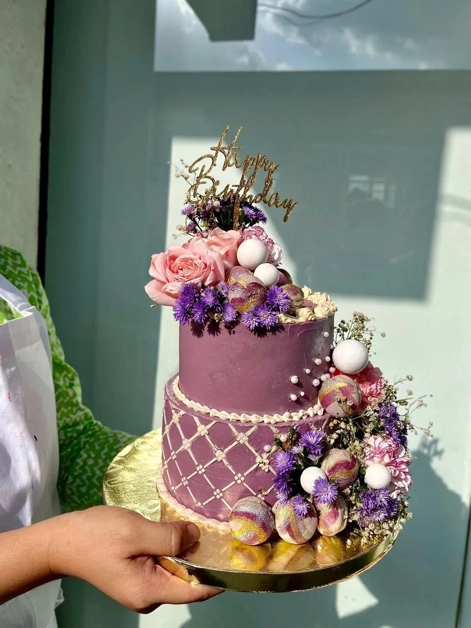 Two-tier purple celebration cake with fresh flowers and macarons