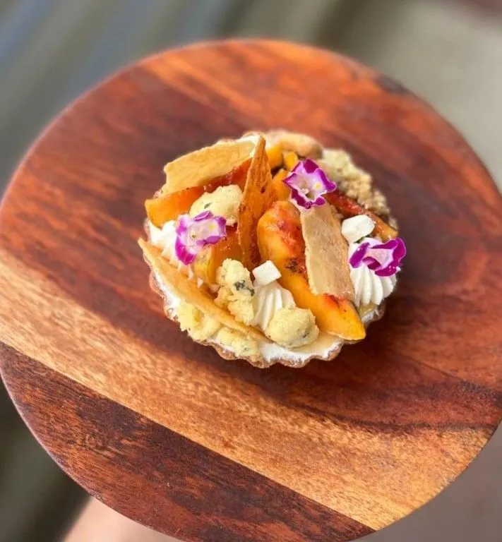 Fruit tartlet topped with cream, crisp tuile and edible flowers